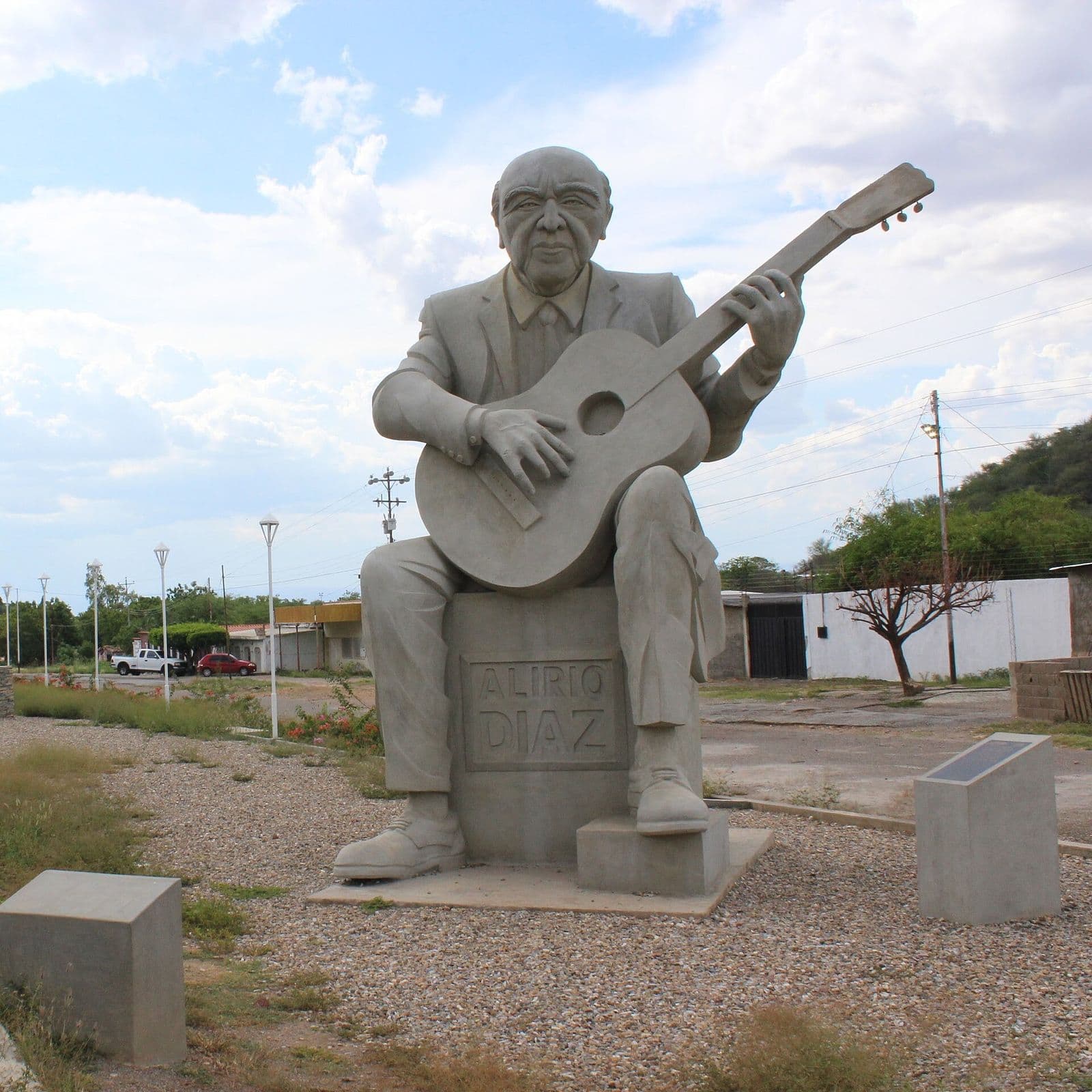 Stone statue of Alirio Díaz seated with his guitar, at the entrance to Carora