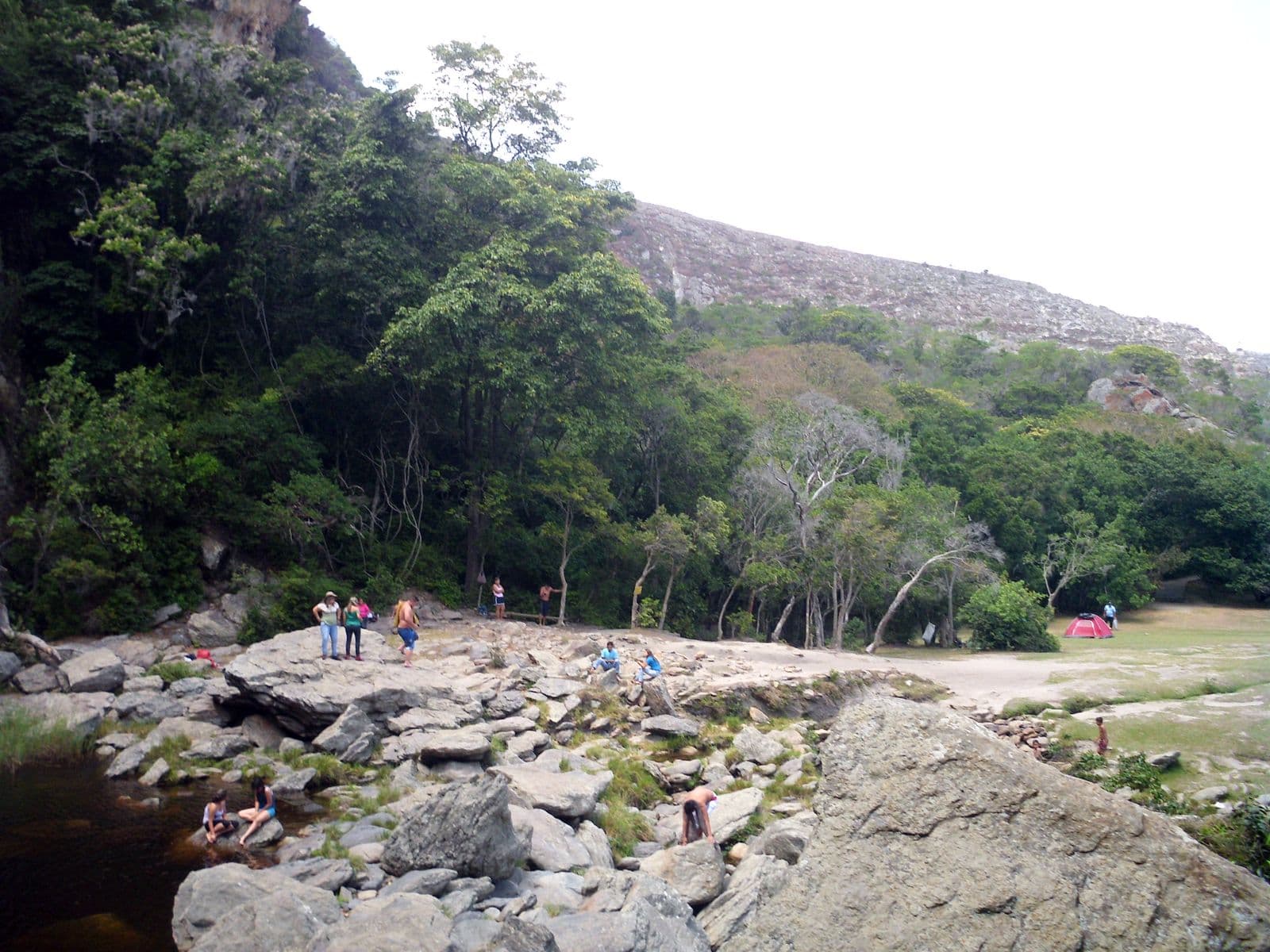 Swimmers on the rocks beside the pool of the Cascada del Vino, below a mountain slope