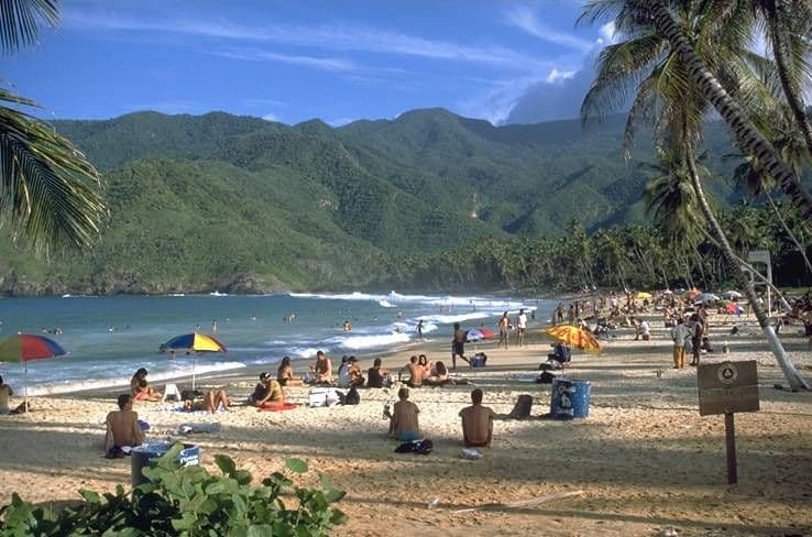 Choroní beach with swimmers and umbrellas, and the green coastal mountains behind