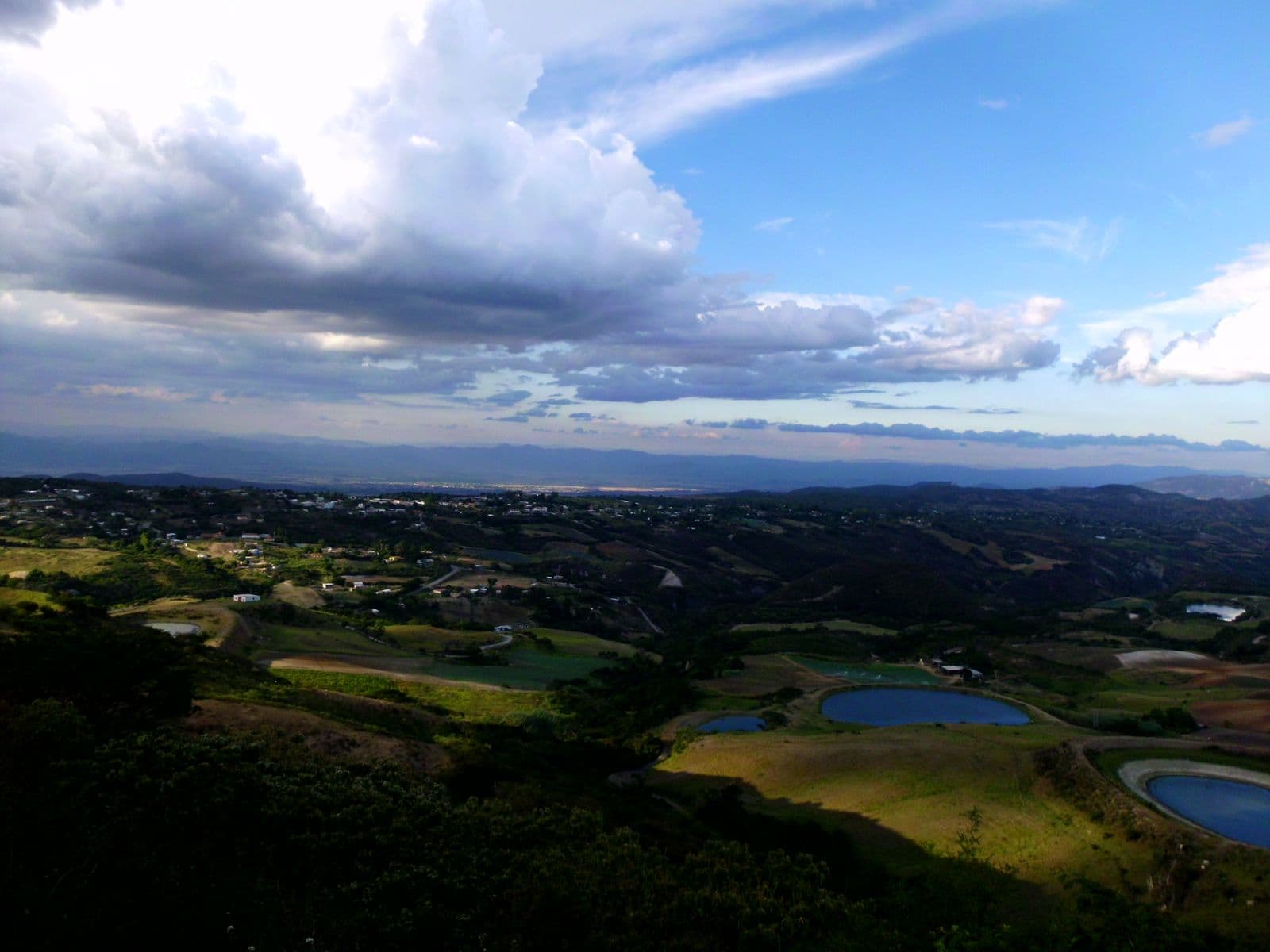 Green hills of Cubiro with small ponds and the valley beyond under a cloudy sky