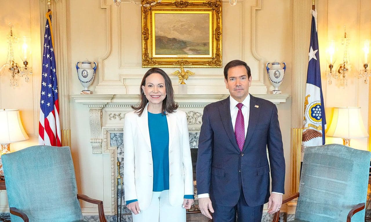 María Corina Machado and Marco Rubio stand in front of a fireplace, between a U.S. flag and the State Department flag.