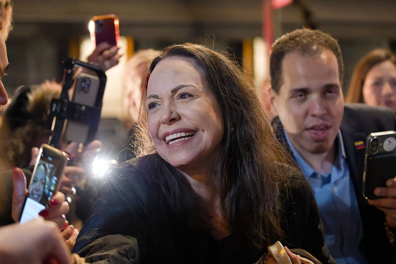 María Corina Machado smiles at night among a crowd filming her on their phones outside Oslo's Grand Hotel.