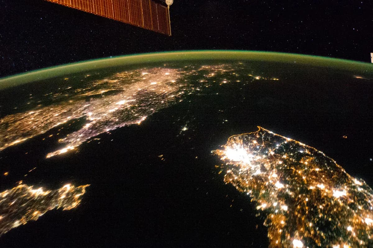 Night photo of the Korean Peninsula taken from space: South Korea shines with lights, especially Seoul; North Korea is almost all dark, with just a small dot of light at its capital; across the sea, China shines too.